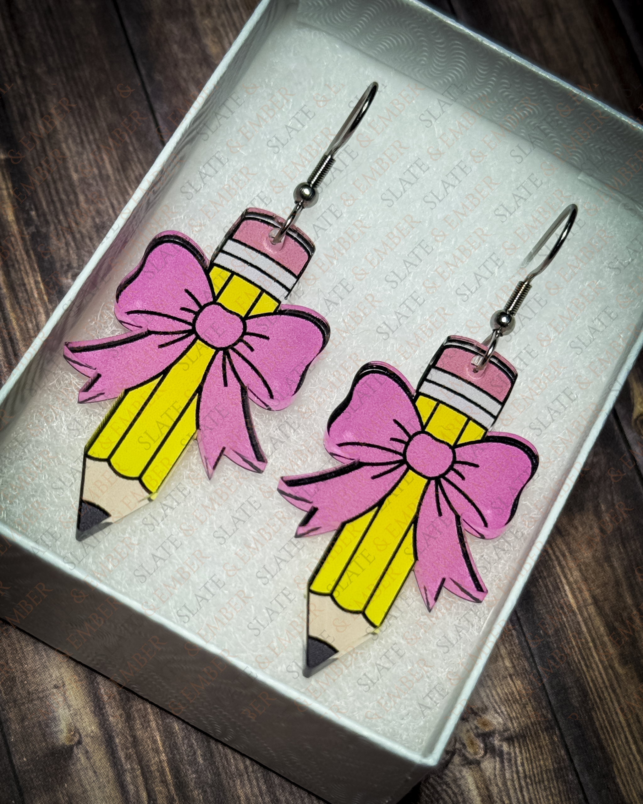 Yellow pencil acrylic earrings with pink bows and silver hook hardware displayed inside a premium white Slate & Ember jewelry gift box.