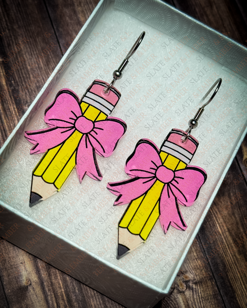 Yellow pencil acrylic earrings with pink bows and silver hook hardware displayed inside a premium white Slate & Ember jewelry gift box.