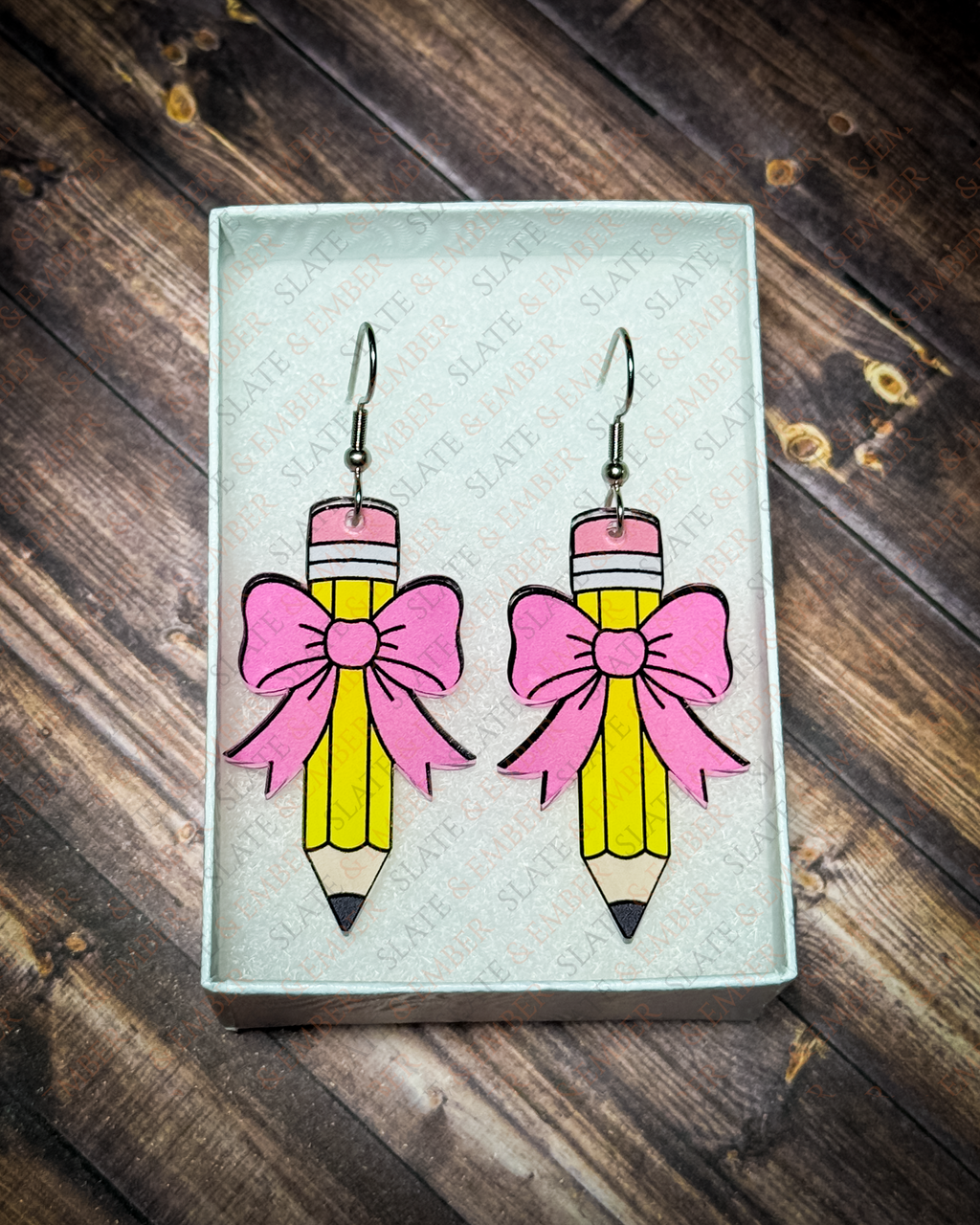 Yellow pencil acrylic earrings with pink bows and silver hook hardware displayed inside a premium white Slate & Ember jewelry gift box.