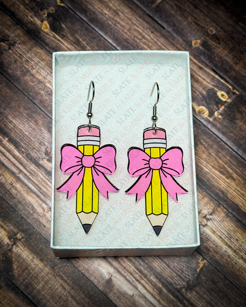 Yellow pencil acrylic earrings with pink bows and silver hook hardware displayed inside a premium white Slate & Ember jewelry gift box.