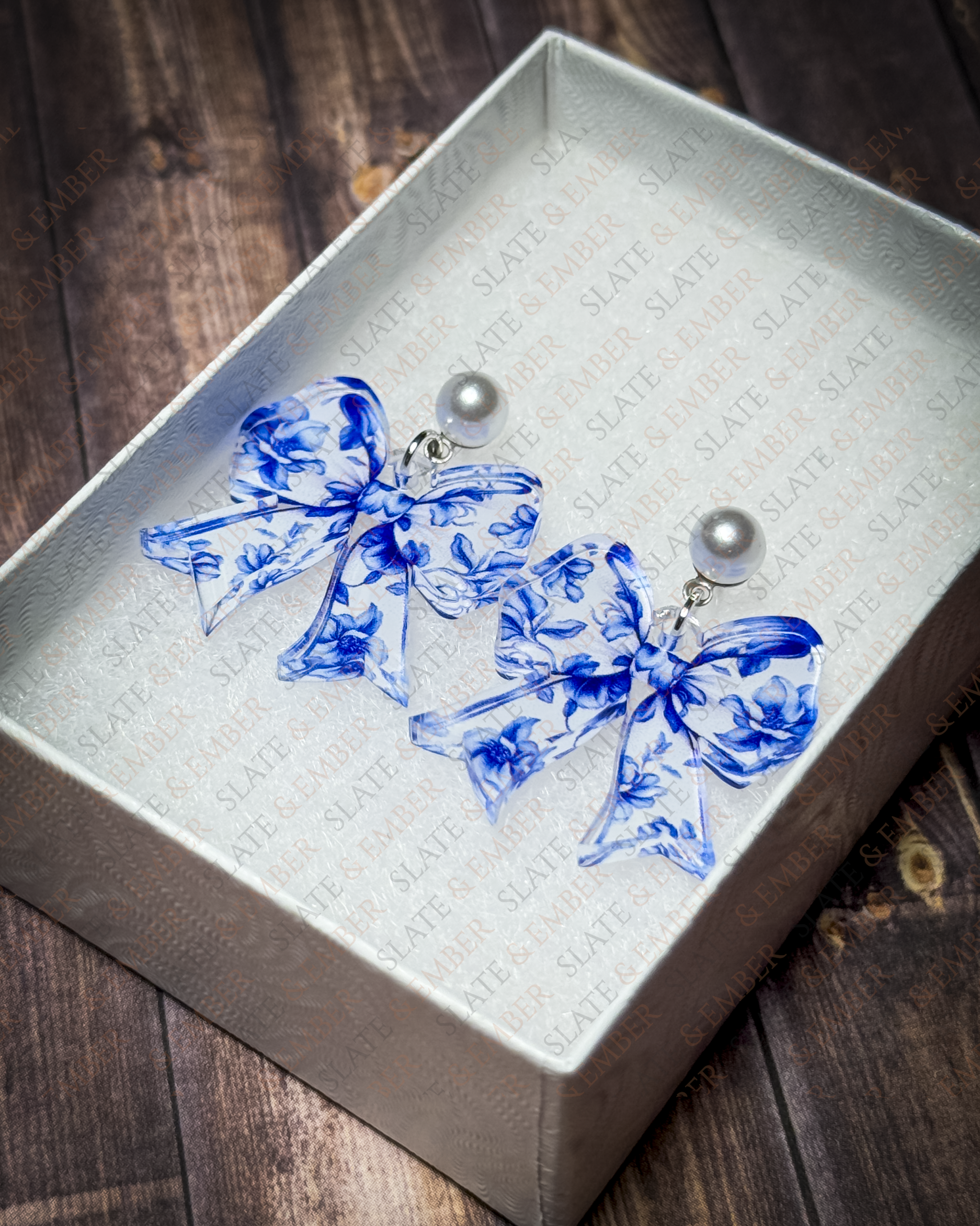 Blue floral chinoiserie acrylic bow earrings with pearl stud tops displayed in a premium white Slate & Ember jewelry gift box.