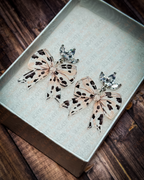 Neutral cow print acrylic bow earrings with crystal leaf stud tops displayed inside a premium white Slate & Ember jewelry gift box.