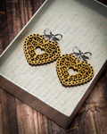 Laser-cut wooden filigree heart earrings with open scrollwork and silver bow stud tops displayed inside a white Slate & Ember jewelry gift box.