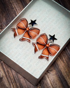 Football bow acrylic earrings with silver star stud tops displayed inside a premium white Slate & Ember jewelry gift box.