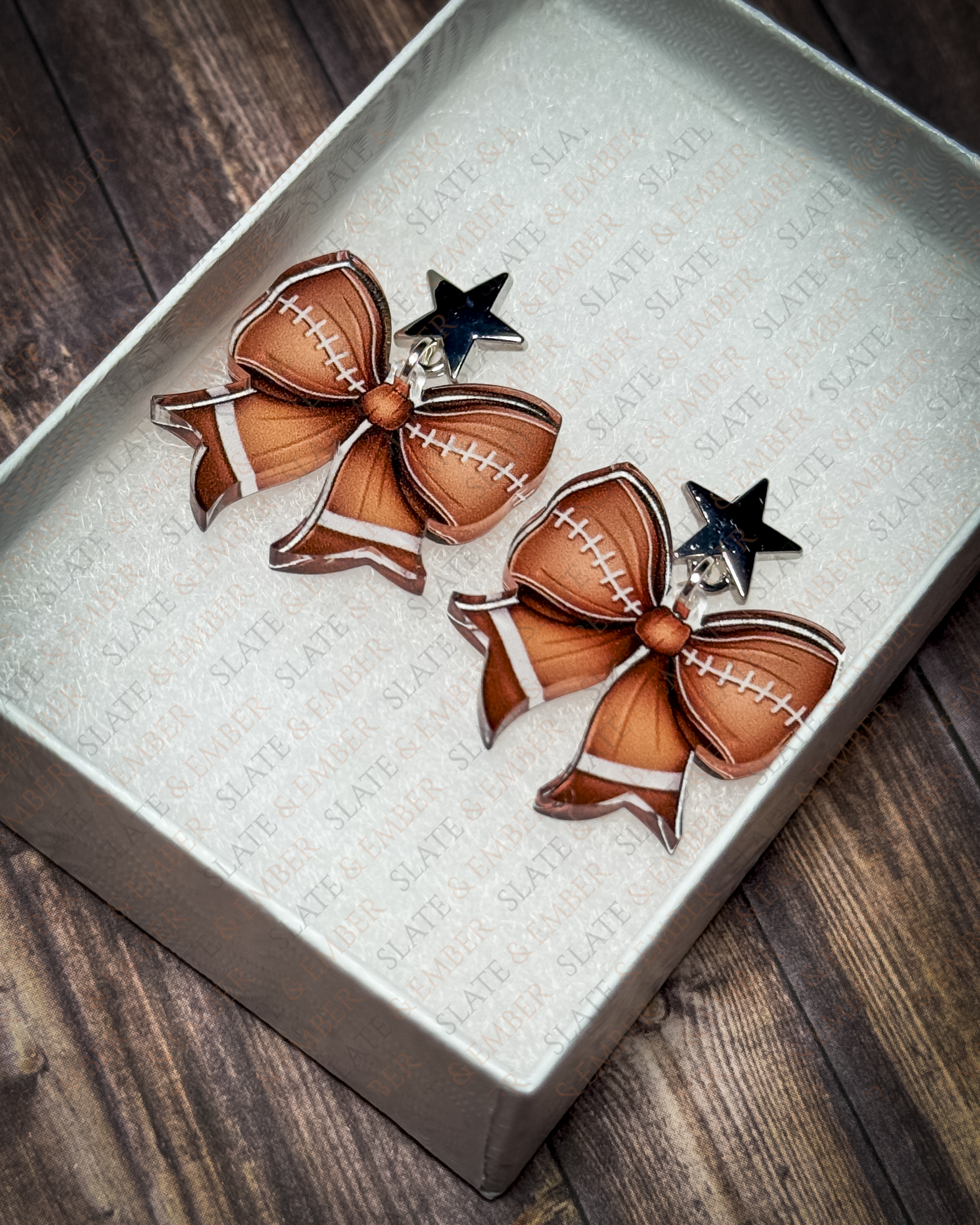 Football bow acrylic earrings with silver star stud tops displayed inside a premium white Slate & Ember jewelry gift box.