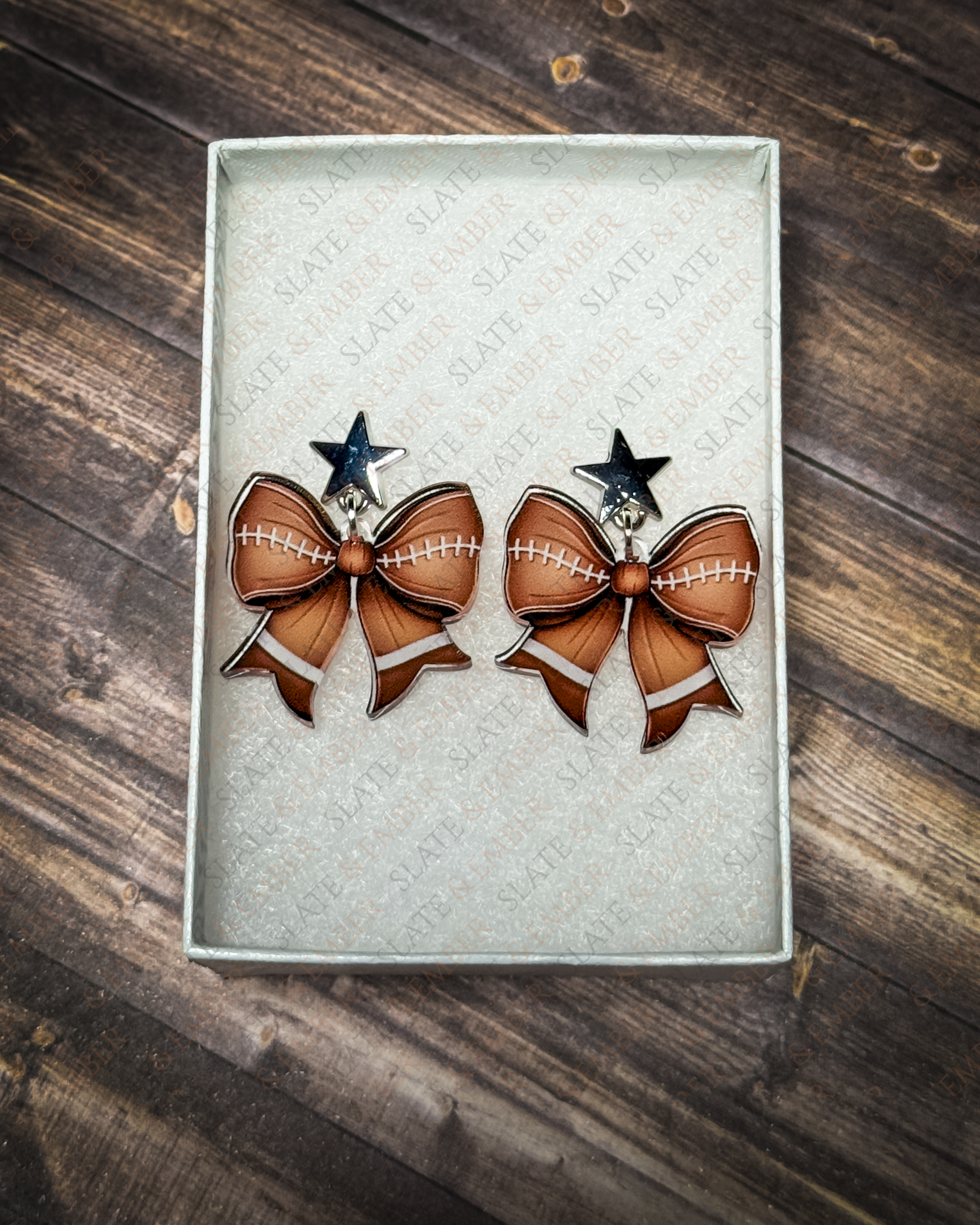Football bow acrylic earrings with silver star stud tops displayed inside a premium white Slate & Ember jewelry gift box.