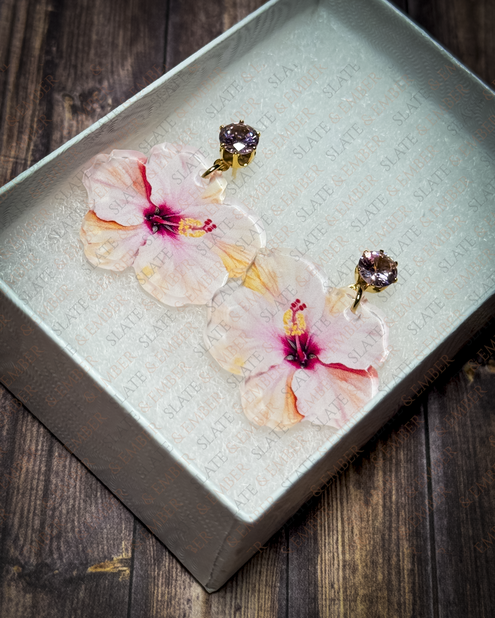 Pink watercolor hibiscus acrylic earrings with pink crystal gold stud tops displayed inside a premium white Slate & Ember jewelry gift box.