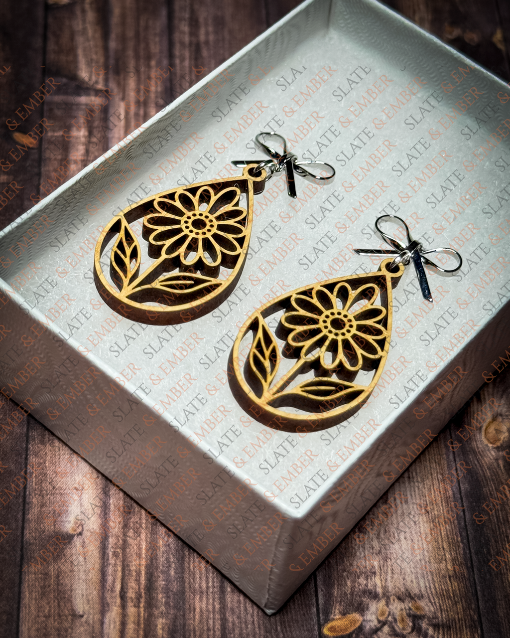 Laser-cut wooden teardrop earrings featuring openwork wildflowers and leaves with silver bow stud tops inside a white Slate & Ember gift box.