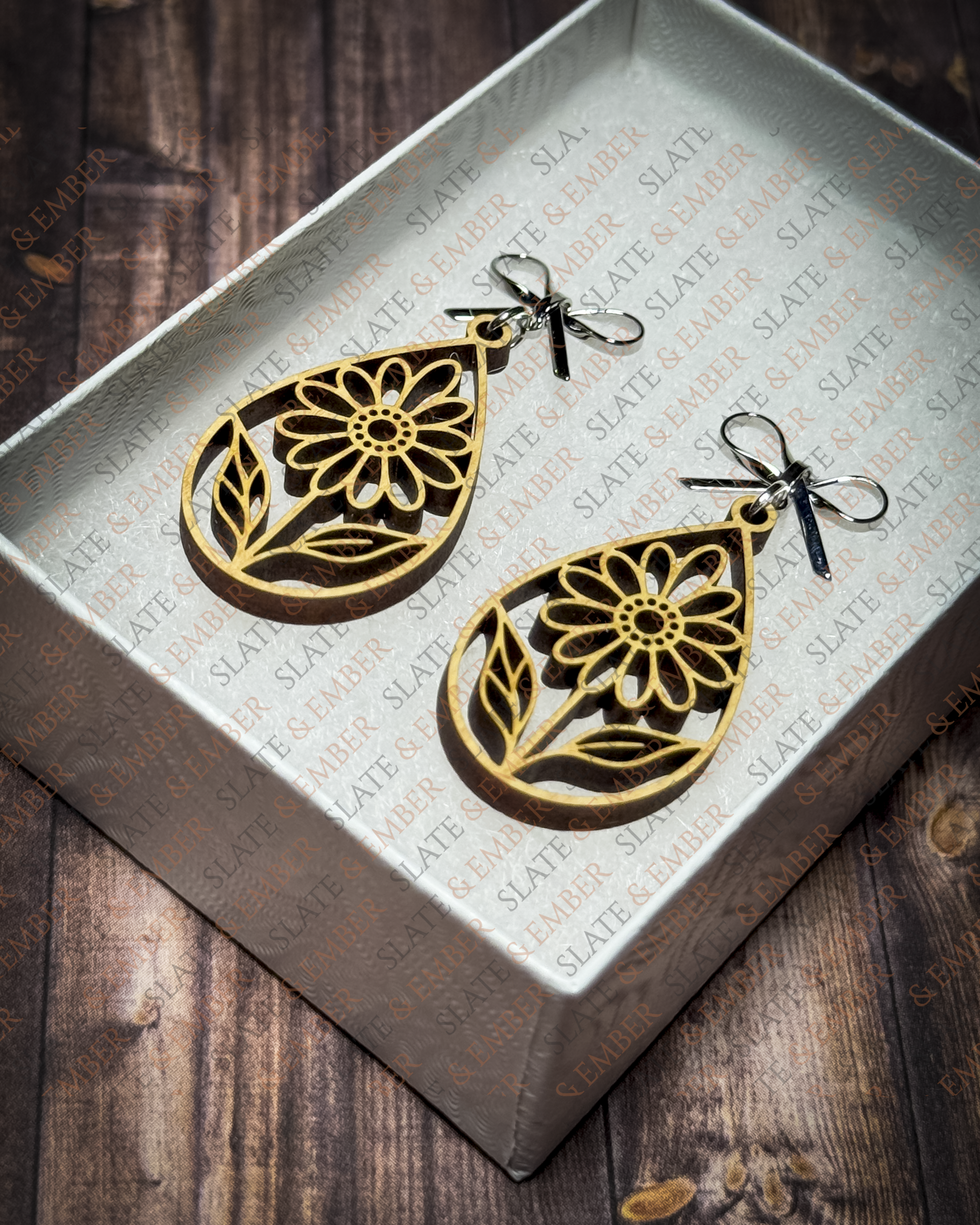Laser-cut wooden teardrop earrings featuring openwork wildflowers and leaves with silver bow stud tops inside a white Slate & Ember gift box.