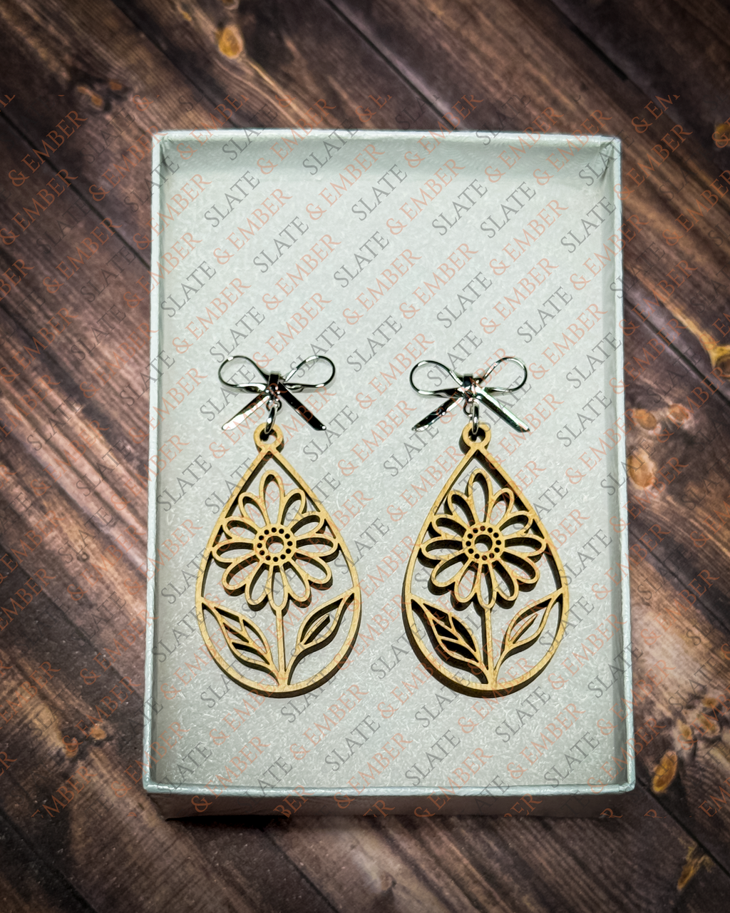 Laser-cut wooden teardrop earrings featuring openwork wildflowers and leaves with silver bow stud tops inside a white Slate & Ember gift box.