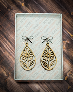 Laser-cut wooden teardrop earrings featuring openwork wildflowers and leaves with silver bow stud tops inside a white Slate & Ember gift box.