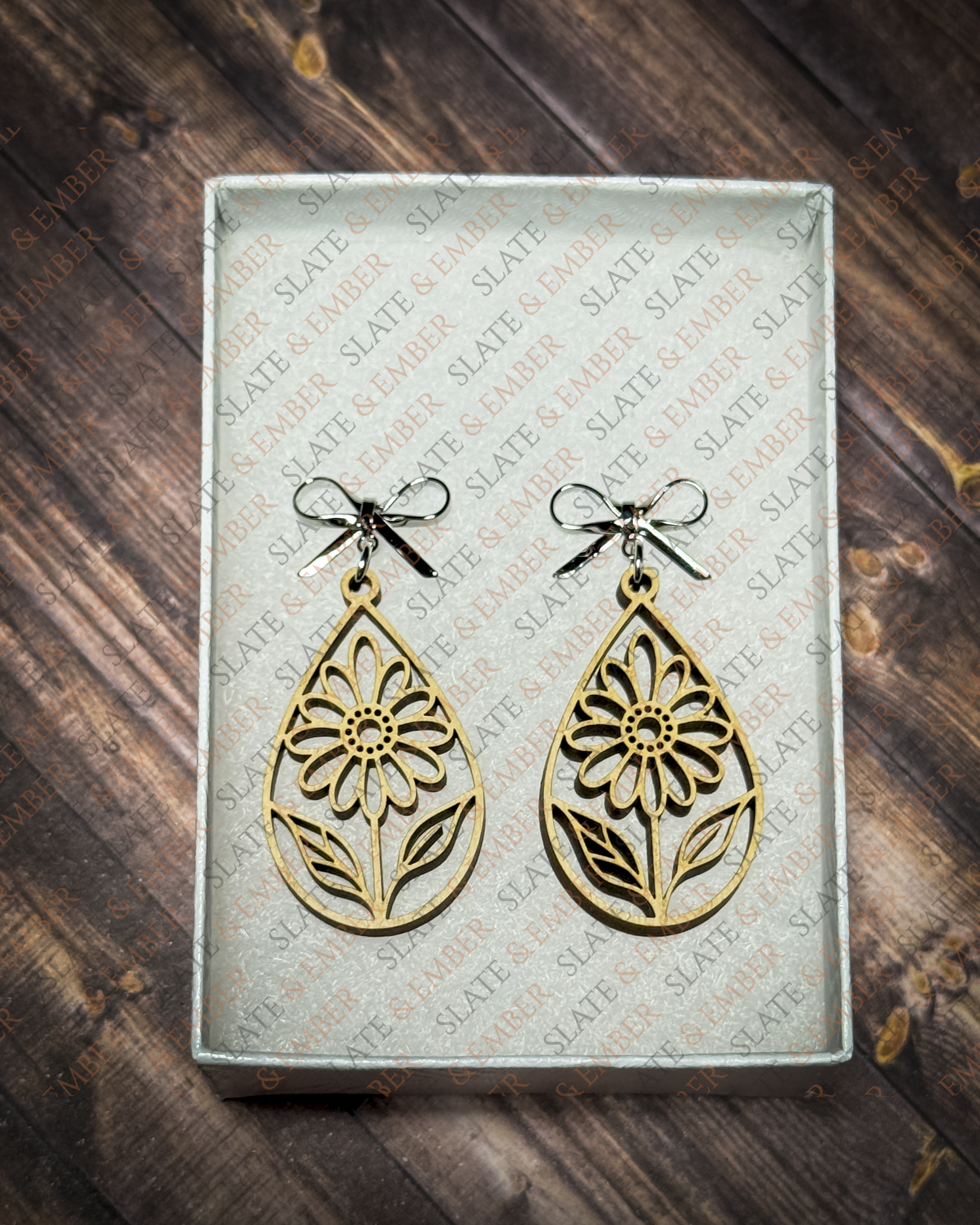 Laser-cut wooden teardrop earrings featuring openwork wildflowers and leaves with silver bow stud tops inside a white Slate & Ember gift box.