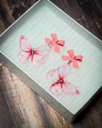 Pink watercolor butterfly acrylic earrings with pink bow stud tops displayed inside a premium white Slate & Ember jewelry gift box.