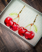 Red cherry acrylic earrings with gold hook hardware displayed inside a premium Slate & Ember jewelry gift box.