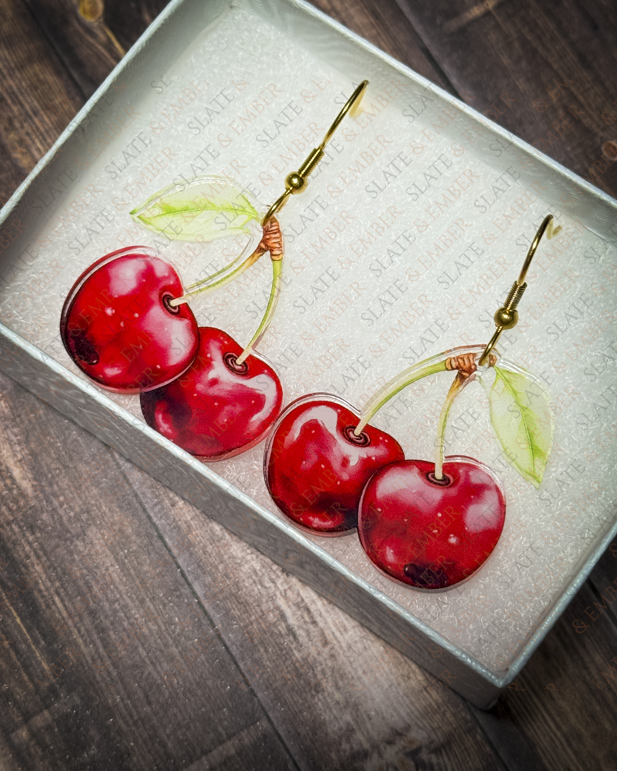 Red cherry acrylic earrings with gold hook hardware displayed inside a premium Slate & Ember jewelry gift box.