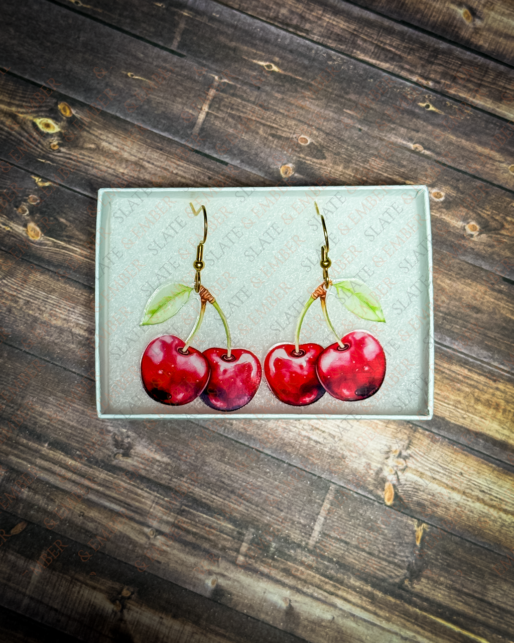 Red cherry acrylic earrings with gold hook hardware displayed inside a premium Slate & Ember jewelry gift box.