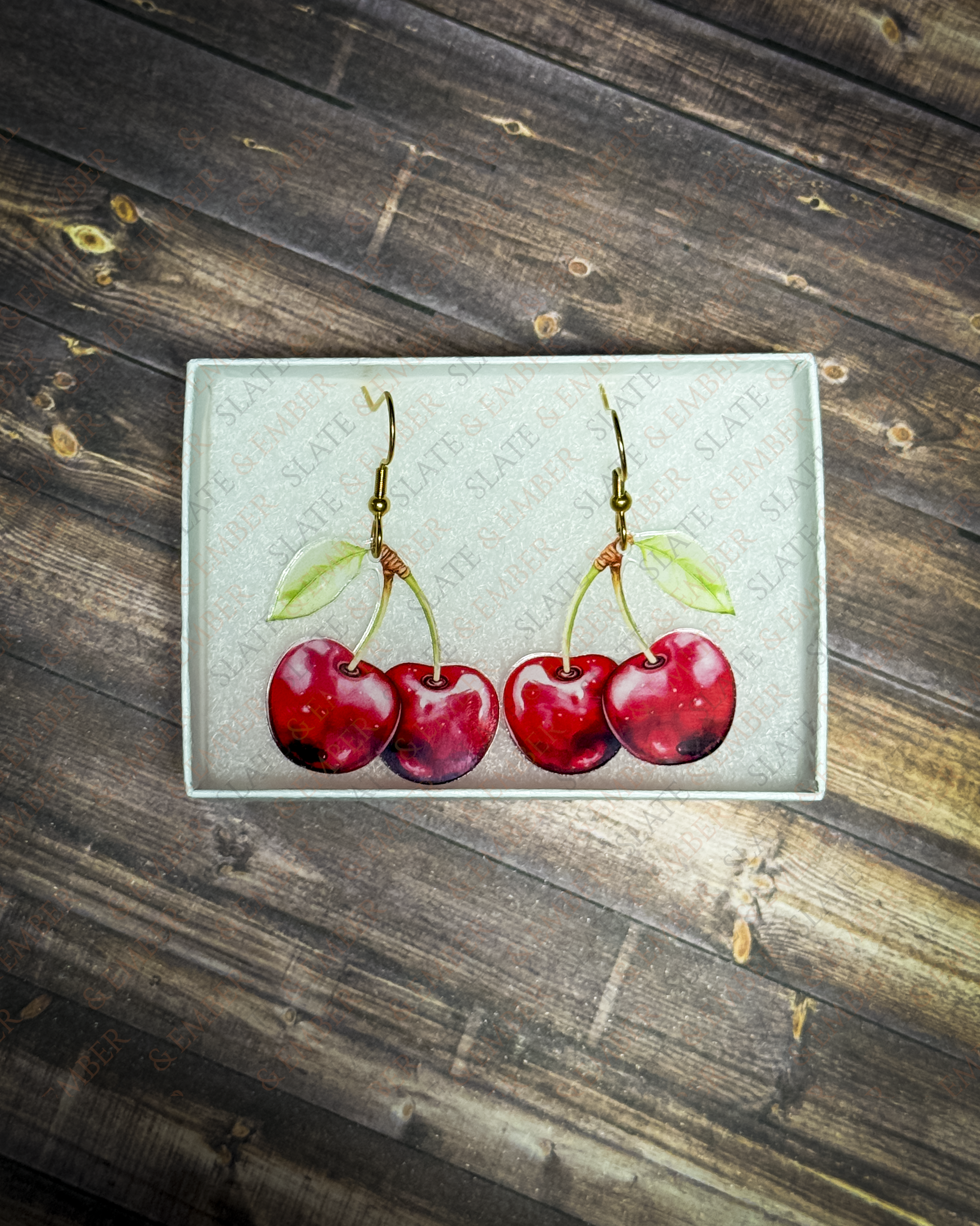 Red cherry acrylic earrings with gold hook hardware displayed inside a premium Slate & Ember jewelry gift box.