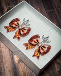 Brown western floral bow acrylic earrings with rose and golden flower details and crystal leaf stud tops displayed inside a white jewelry gift box.